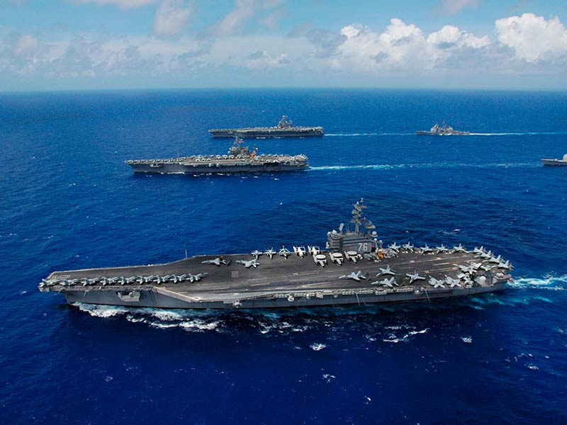 Photo of the Nimitz-class aircraft carrier USS Ronald Reagan (foreground), the USS Kitty Hawk (center), USS Abraham Lincoln, and their associated carrier strike groups steam in formation, participating in exercise Valiant Shield 2006.